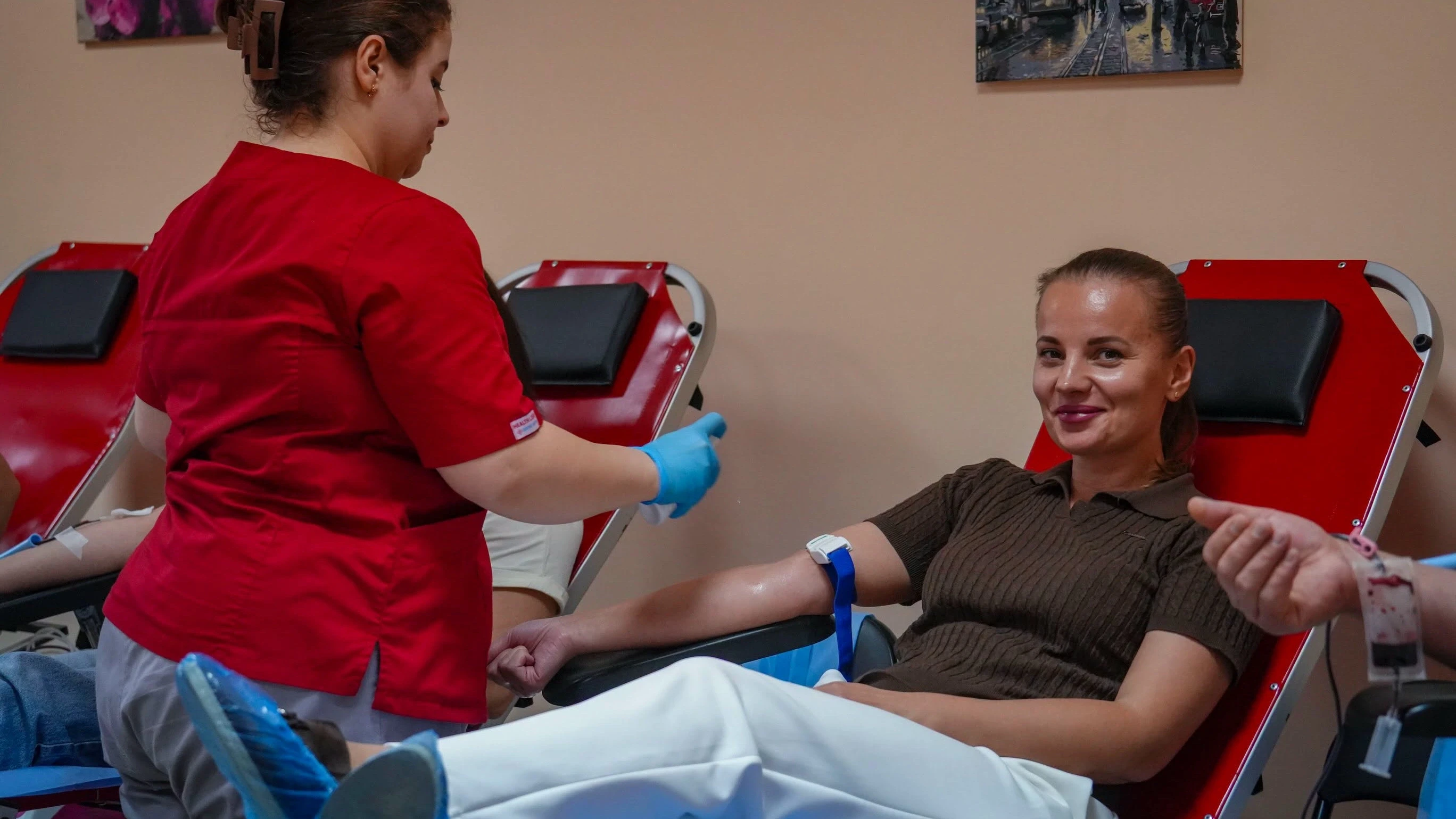 Донорка в кріслі під час здачі крові, поруч медсестра